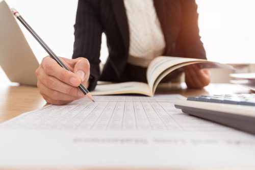 A person writing on paper with a pen and calculator.